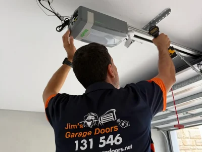 Garage door opener installation with technician adjusting motor unit and rail system inside residential garage